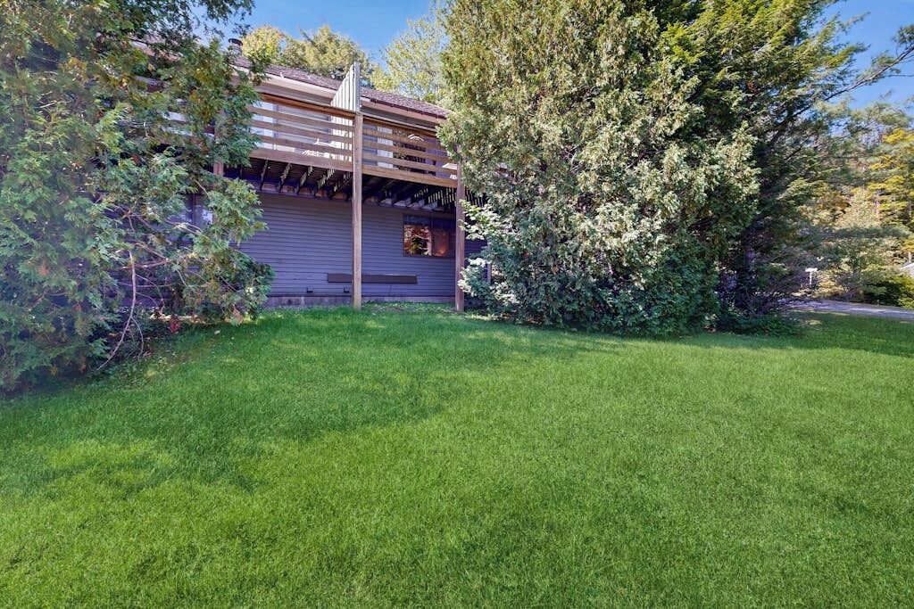 Ein Haus mit überdachter Veranda, einem gepflegten Rasen und umliegenden Bäumen.