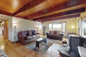 Ein geräumiges Wohnzimmer mit Holzbalken, zwei Sofas, einem Kamin und einem großen Fenster.