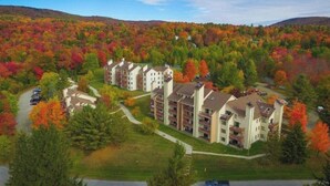 A multi-story residential building with a central courtyard, surrounded by a forested area with autumn foliage. - Cozy condo on Moover route w/ amazing views, fireplace, balcony, hot tubs, pool (Dover)