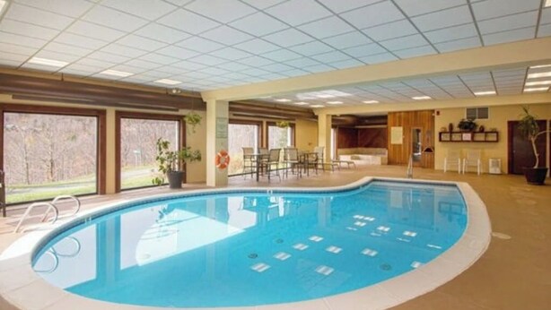 An indoor swimming pool with clear blue water, surrounded by a tiled floor and walls, and equipped with a lifeguard chair. - Cozy condo on Moover route w/ amazing views, fireplace, balcony, hot tubs, pool (Dover)