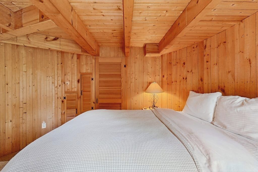 A wooden-paneled room with a bed, a lamp, and a door.