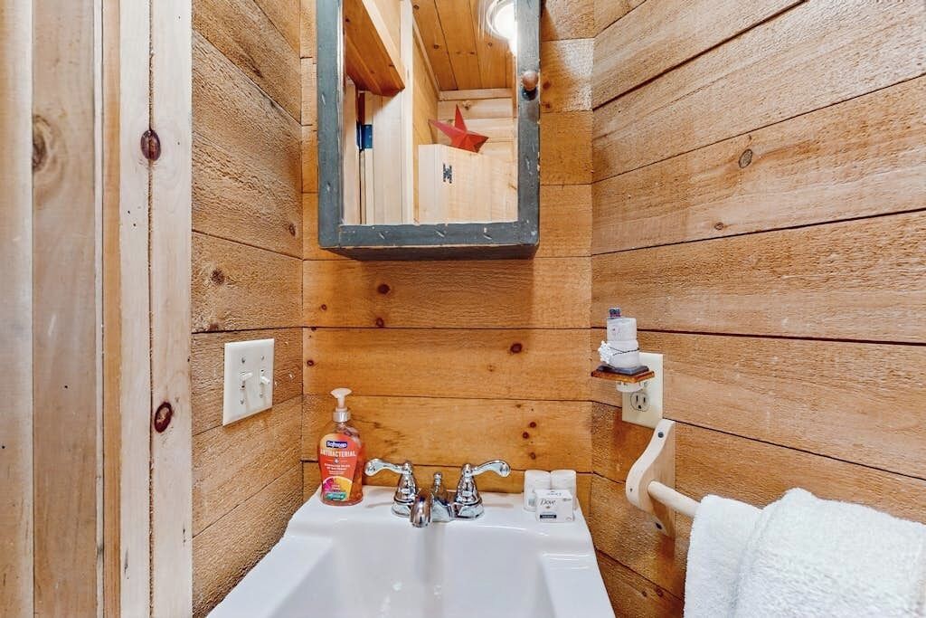 A wooden cabin bathroom with a sink, mirror, and toiletries.