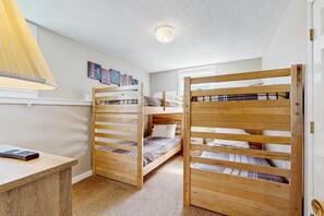 Una habitación con literas, un escritorio, una lámpara y una pared con ilustraciones coloridas.