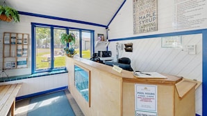 Zona de recepción con mostrador, un cartel que indica los horarios de la piscina y vistas al exterior.