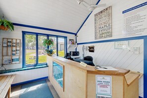 Zona de recepción con mostrador, un cartel que indica los horarios de la piscina y vistas al exterior.
