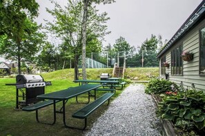Eine Terrasse mit Picknicktischen, einem Grill und einem Haus mit überdachter Veranda.