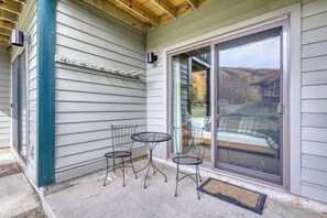 Un patio techado con sillas y una mesa de metal, una puerta corrediza de vidrio y una barandilla metálica.