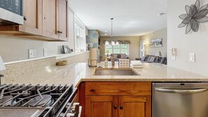 Una cocina con encimeras de granito, armarios de madera, lavavajillas de acero inoxidable y estufa a gas.