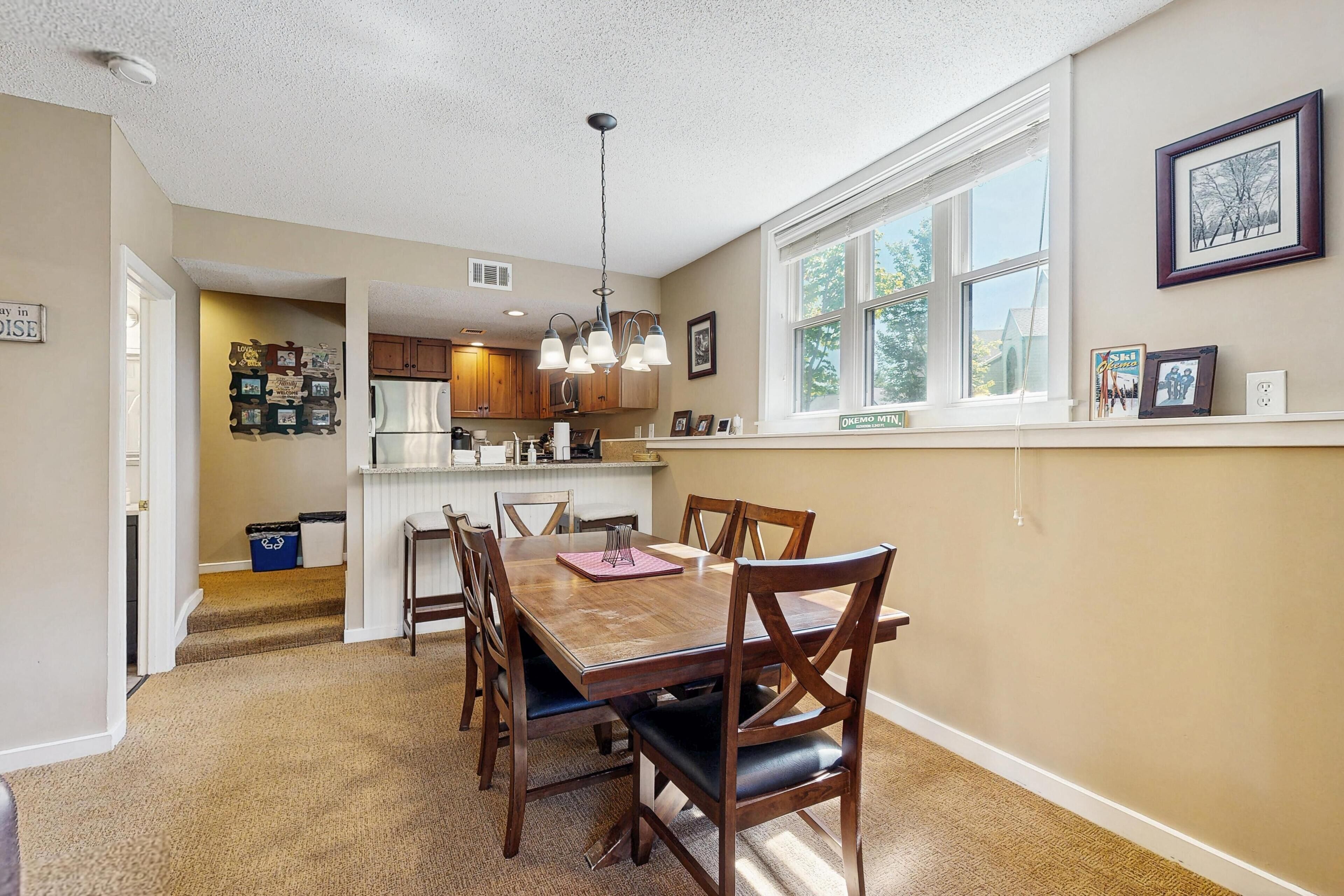 A dining area with a wooden table and chairs, a kitchen with wooden cabinets, and a window with a view.