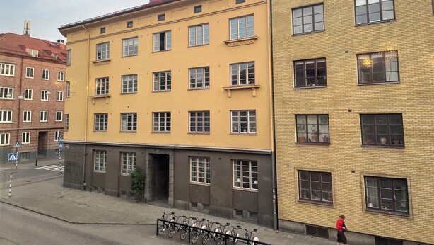 A multi-story building with a yellow facade, multiple windows, and a visible entrance. - Cozy flat in a quiet, leafy neighborhood in central Malmö (Malmö)