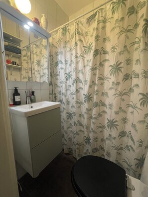 A bathroom with a toilet, sink, mirror, and shower curtain with a palm tree pattern.