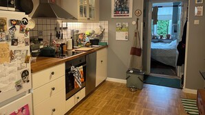 A kitchen with a microwave, stove, and various kitchen utensils. There is a calendar on the wall and a door leading to another room. - Cozy flat in a quiet, leafy neighborhood in central Malmö (Malmö)