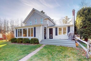 A two-story house with a front porch, a chimney, and a covered entryway. - Cozy dog-friendly home, fenced yard, gas fireplace, BBQ, wifi, partial a/c, w/d (Dorset)