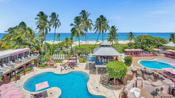 Ein Resort mit großem Pool, Liegestühlen, Palmen und Blick auf den Strand.