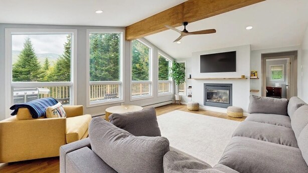 A modern living room with large windows, a fireplace, and a ceiling fan. - Beautiful house w/ mountain views, fireplace, balcony, bbq, gameroom, w/d, a/c (Dover)