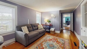 A living room with a grey sofa, a patterned rug, and a wooden floor. - Central home: near town, lake, skiing, rail trial, snowshoe from your door (Wolfeboro)