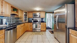A kitchen with wooden cabinets, stainless steel appliances, and a tiled backsplash. - Central home: near town, lake, skiing, rail trial, snowshoe from your door (Wolfeboro)