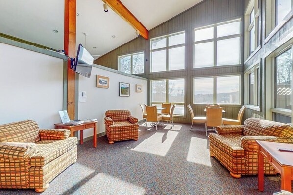 Ein geräumiges Zimmer mit großen Fenstern, einem Fernseher und einem karierten Sofa.