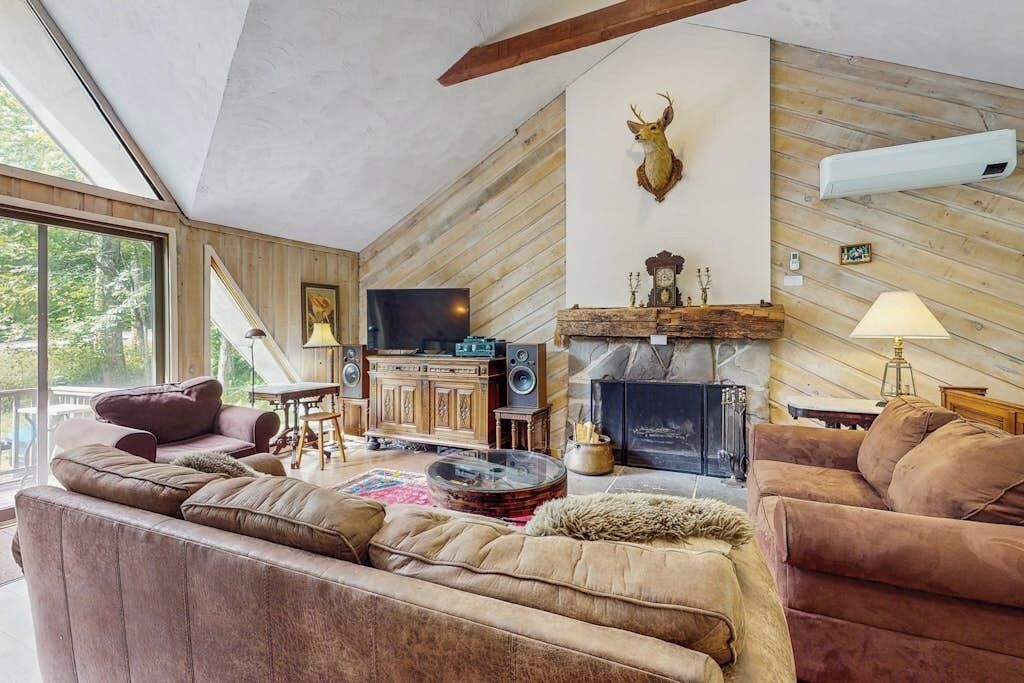 A cozy living room with a fireplace, leather sofas, a mounted deer head, and a television.