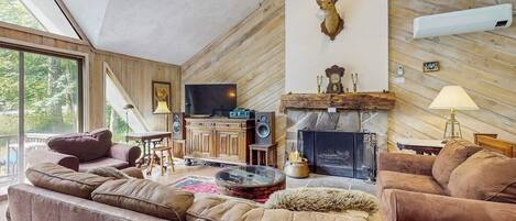 A cozy living room with a fireplace, leather sofas, a mounted deer head, and a television.