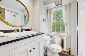 Une salle de bain avec un double lavabo, des toilettes, une fenêtre avec des rideaux et un radiateur.