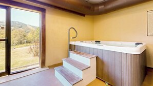 Een spa-ruimte met een bubbelbad, houten trap en uitzicht door een glazen deur.