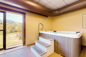 Ein Wellnessraum mit Whirlpool, Holzstufen und Blick durch eine Glastür.