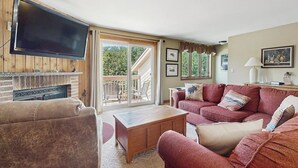 Een woonkamer met een televisie, open haard, bank en een balkon met tuinmeubilair.