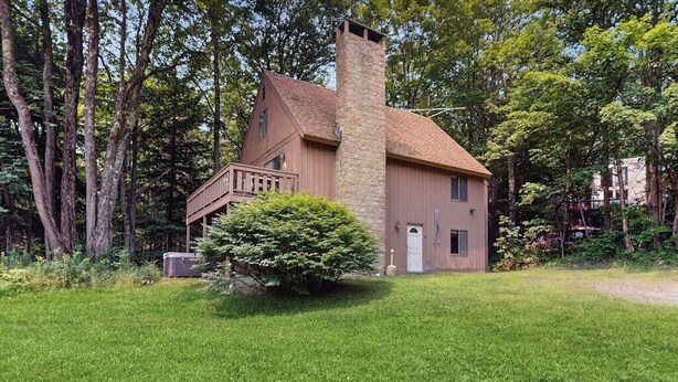 Une maison à deux étages avec une cheminée en pierre, un petit porche et une pelouse bien entretenue.