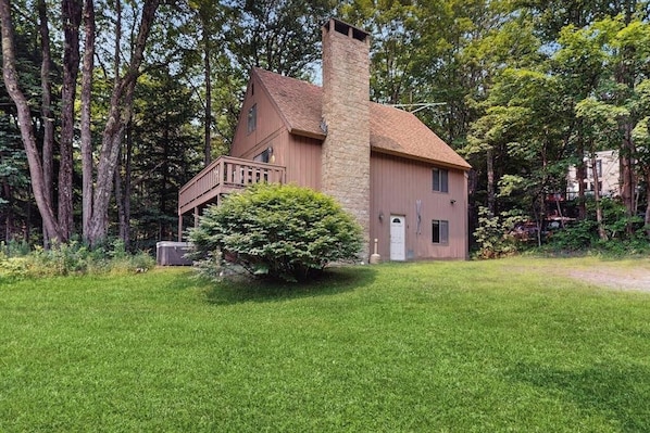Ein zweistöckiges Haus mit einem Steinsschornstein, einer kleinen Veranda und einem gepflegten Rasen.