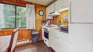 Une cuisine de style rustique, avec des murs en bois, un poêle, un évier, des placards et une fenêtre agrémentée de rideaux.
