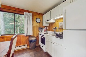 Eine Küchenzeile in einer Holzhütte, mit Herd, Spüle, Schränken und einem Fenster mit Vorhängen.