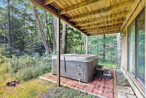 Ein Whirlpool unter einer hölzernen Pergola in bewaldeter Landschaft.