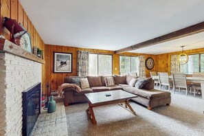 Ein gemütliches Wohnzimmer mit Kamin, einer großen Couch, einem Couchtisch und einem Essbereich mit Tisch und Stühlen.