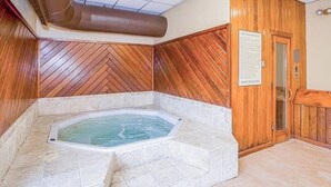 Un bain à remous installé dans un coin, avec un revêtement mural en bois et un panneau d’avertissement.