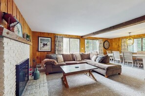 Ein gemütliches Wohnzimmer mit Kamin, Holzwänden, einer Eckcouch und einem Essbereich mit Tisch und Stühlen.