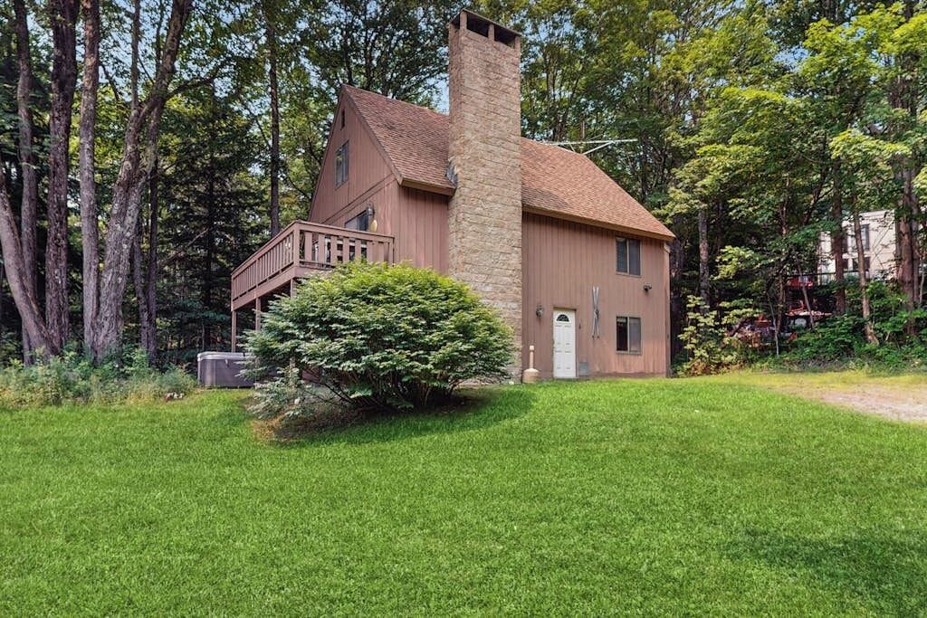 Kaksikerroksinen talo, jossa on kivinen savupiippu, puinen terassi ja hyvin hoidettu nurmikko.