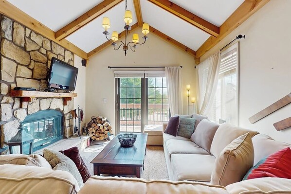 Ein gemütliches Wohnzimmer mit Kamin aus Stein, Fernseher, Sofa und einer Chandelier.