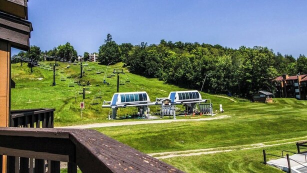 A view of a grassy area with a ski lift and a building in the background. - Ski-in/out mountainside condo close to everything with full kitchen - tranquil (Ludlow)