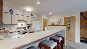 A kitchen with a long counter, wooden stools, a refrigerator, and a clock on the wall. - Ski-in/out mountainside condo close to everything with full kitchen - tranquil (Ludlow)