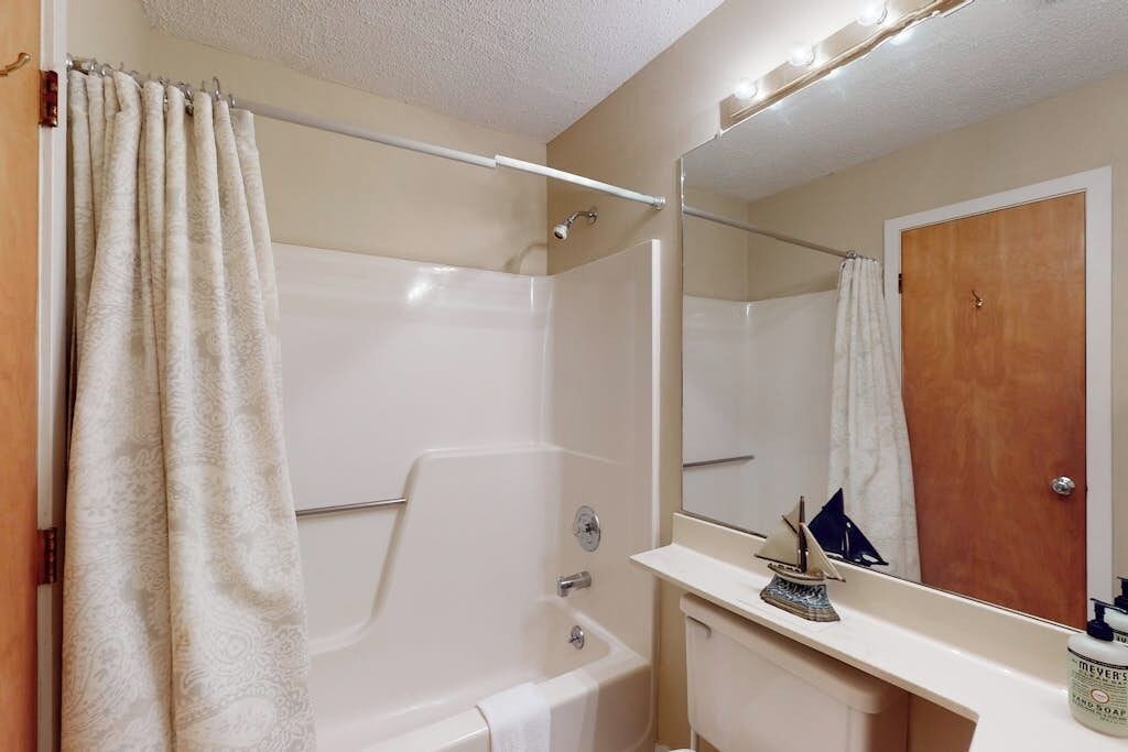 Un baño con bañera, tocador con espejo y cortina de ducha.