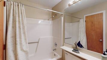 Un baño con bañera, tocador con espejo y cortina de ducha.