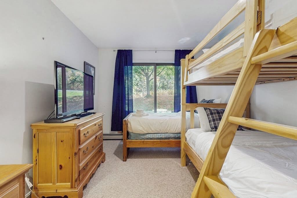 A bedroom with bunk beds, a television on a dresser, and a window with curtains.