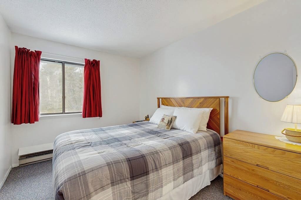 Une chambre à coucher avec un lit, une commode, un miroir et une fenêtre avec des rideaux.
