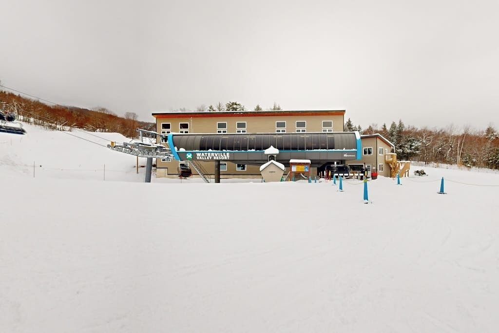 Un edificio con la scritta 'Waterville Valley Resort', una seggiovia e paesaggi innevati.