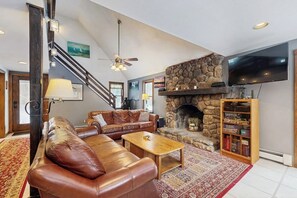 Een woonkamer met een stenen openhaard, leren bank, houten salontafel en een boekenkast.