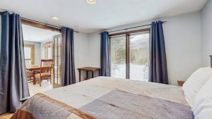 Une chambre avec un grand lit, une petite table et une chaise. Une porte coulissante donne sur un balcon.