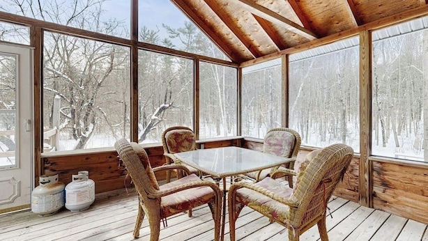 Eine Holzterrasse mit Glasverkleidung, Korbstühlen, einem Glastisch und Propangasflaschen.