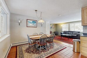 A dining area with a wooden table and chairs, a red patterned rug, a sofa, and a trash can. - White Mountain home w/ yard near skiing, hiking & tubing (Campton)