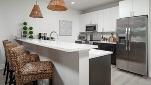 Een moderne keuken met een centraal eiland, roestvrijstalen apparatuur, rieten stoelen en hanglampen.